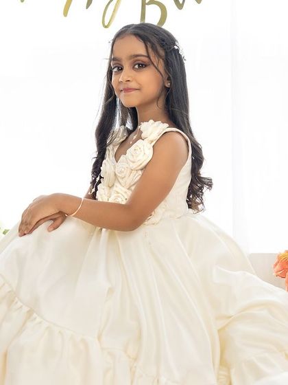 An elegant portrait of a seven-year-old girl in a beautiful white gown, seated amidst flowers and balloons for her birthday.