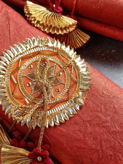 A close-up of our handmade wedding scrolls. This one features a beautiful orange fabric with a traditional gota-patti style emblem, perfect for a royal-themed wedding.