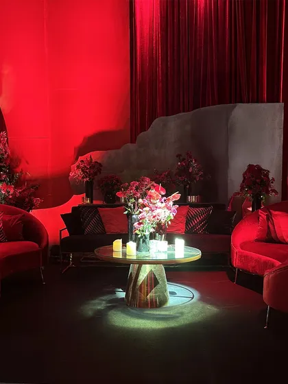 A cozy lounge nook bathed in red light, with plush red velvet seating and modern floral arrangements, creating an intimate space within the larger celebration.