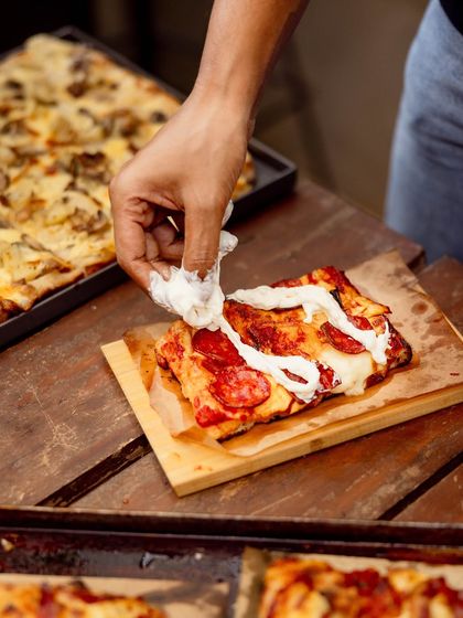 Adding a final touch of creamy stracciatella to a slice of pepperoni Pizza Romana.