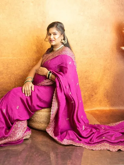 A seated portrait in a beautiful pink saree. The addition of pampas grass in the background adds a modern touch to the traditional setup.