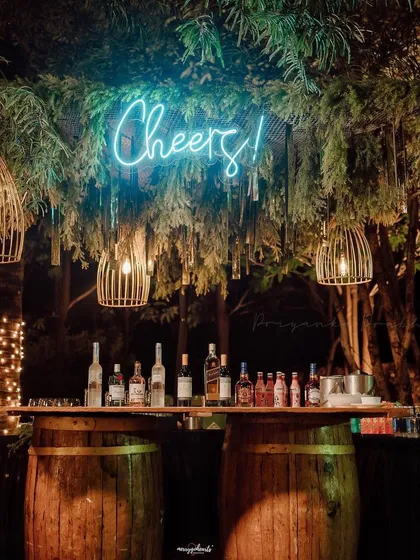 A rustic and minimal bar setup perfect for an outdoor party. We used wooden barrels as the base, a simple wooden countertop, and a 'Cheers!' neon sign nestled in greenery for a cool, relaxed vibe.