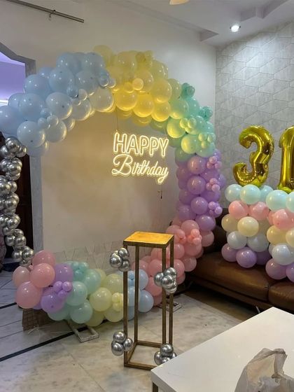 A 31st birthday home setup with a pastel rainbow balloon ring, a neon sign, and foil numbers.