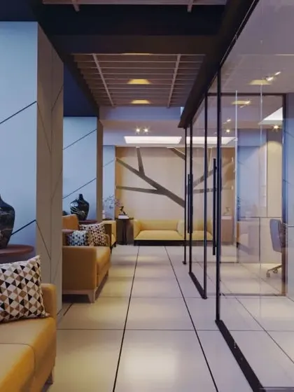 A waiting area and corridor in a modern office, featuring comfortable seating and glass-walled cabins. The design prioritizes natural light and a clean, uncluttered layout to create a pleasant and productive atmosphere.