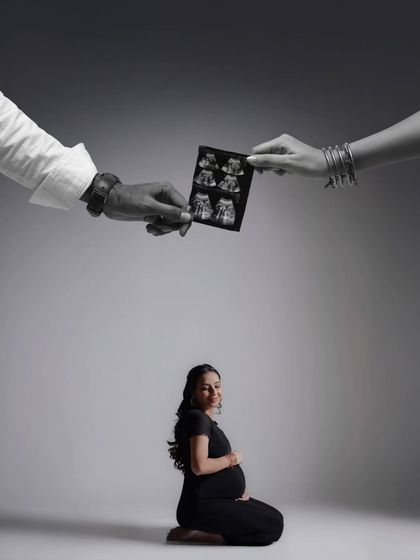 A creative and artistic composition. The parents' hands hold the sonogram above the mother-to-be, symbolizing their joint love and protection over their growing family.