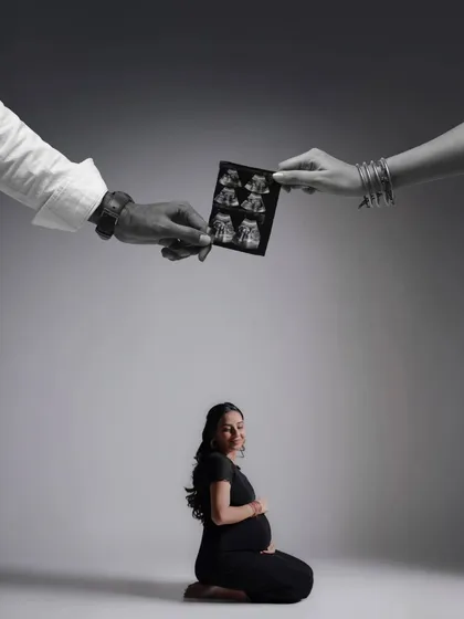 A creative and artistic composition. The parents' hands hold the sonogram above the mother-to-be, symbolizing their joint love and protection over their growing family.