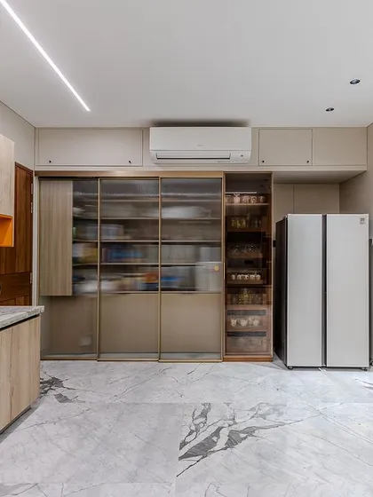 In Dr. Sneha Baxi's Ahmedabad kitchen, a large pantry unit with sliding glass doors and internal pull-outs offers incredible storage capacity and organization.