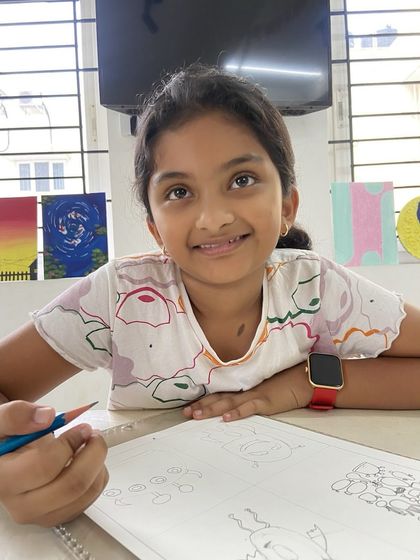 A young artist looks up from her drawing, ready for the next step. Our instructors are always on hand to provide encouragement and guidance, helping students feel confident as they learn.