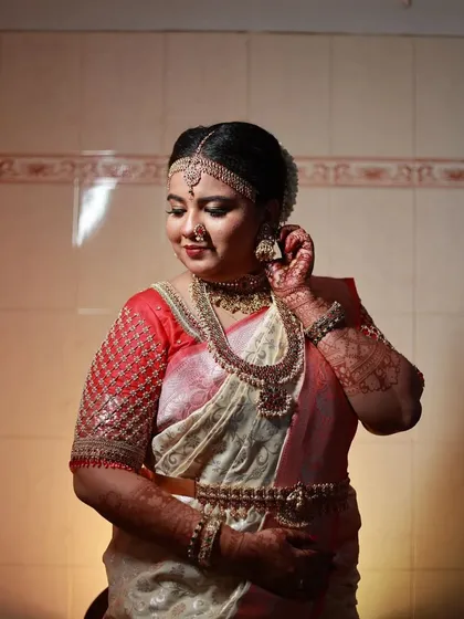 This bride is adjusting her earrings, showing a close-up of the Kempu stones and pearl drops.