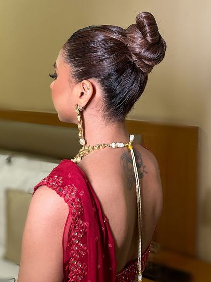 The back view, highlighting the intricate sleek high bun that adds a touch of modern sophistication to the traditional red saree look.