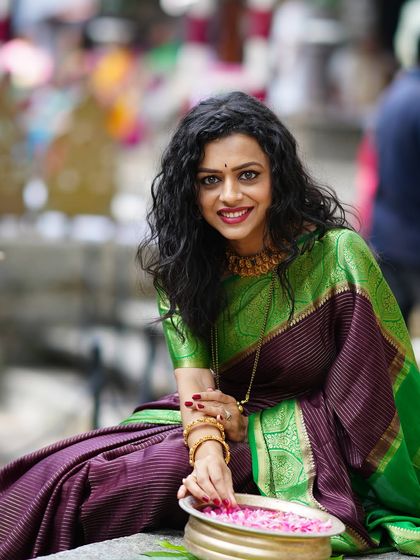 A woman in a gorgeous silk saree enjoying a moment at an outdoor event, with a bowl of flower petals.