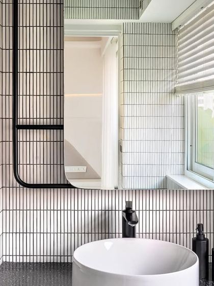 The son's bathroom in Apartment 56 continues the edgy, black-and-white theme. White finger mosaic tiles flow over curved walls to make the compact space feel larger, while matte black fittings provide a sleek, modern contrast.
