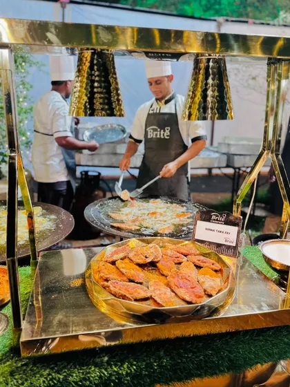 The Surmai Tawa Fry station, with a platter of freshly fried fish in the foreground and a chef cooking in the back.