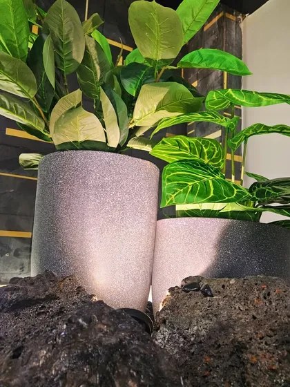 A close-up of the under-staircase pebble garden. The combination of dark pebbles, lava rocks, and high-quality artificial plants in stone-finish pots creates a sophisticated and completely maintenance-free indoor garden.