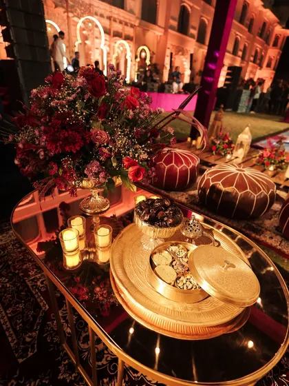 A close-up of a Moroccan-themed coffee table, featuring a brass tray with a 'masala daani' and a bowl of dates. Leather ottomans in the background complete the authentic souk-inspired vibe.