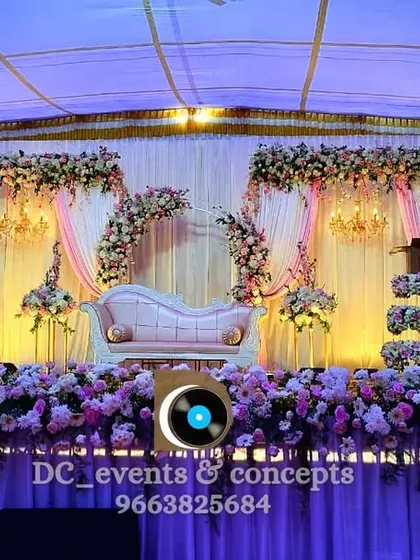 A lovely wedding reception stage setup in soft lavender and pink hues. The design includes a beautiful cake stand and floral arrangements along the front, creating a cohesive and charming look.