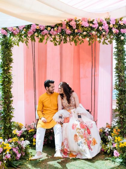 The couple seated on a beautifully decorated floral swing, sharing a sweet moment during their Haldi.