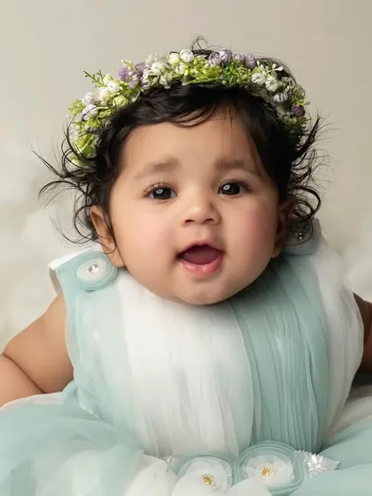 A beautiful close-up portrait of this six-month-old baby, highlighting her bright eyes, curly hair, and delicate floral crown.