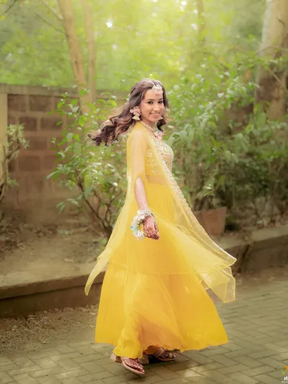 A happy Haldi bride twirling in her yellow outfit, adorned with our fresh flower accessories.