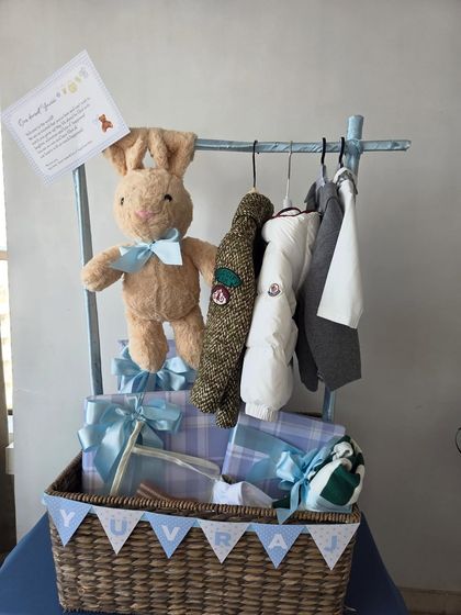 A charming wicker basket hamper featuring a clothing rack with designer baby outfits and a cuddly bunny for baby Yuvraj.