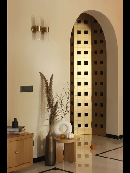 The metallic-finished mandir door, seen through an archway, creates a beautiful play of light and shadow. This custom piece acts as a spiritual and artistic focal point in the home.