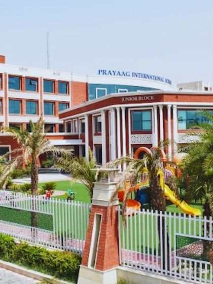 A wider view of the Prayag International School campus, showing the main building and the Junior Block alongside a play area. The cohesive design creates a grand and welcoming educational environment.