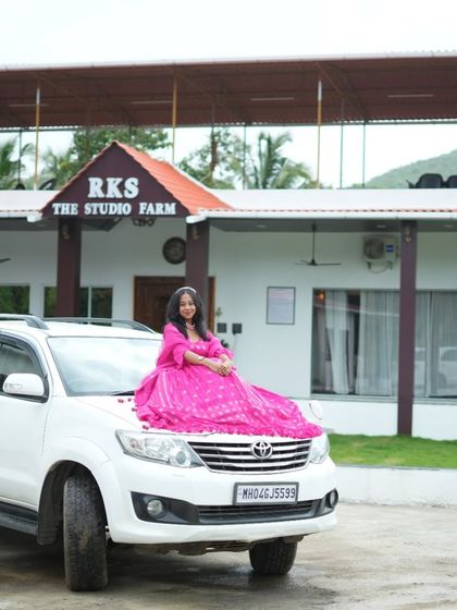 For a dramatic and fun shot, we can get creative at our outdoor locations. Here, a client poses in a vibrant pink gown on top of a car, with the beautiful studio farm building in the background.
