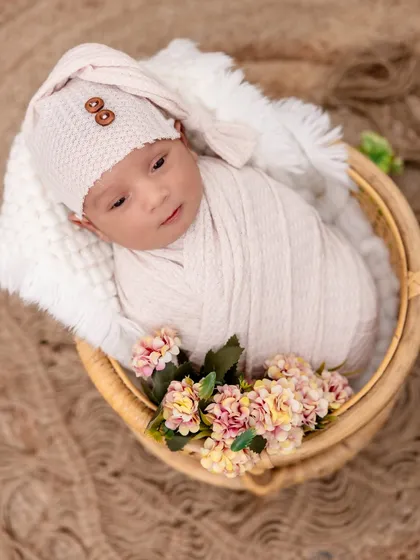 Snuggled in a woven basket with delicate flowers. This newborn portrait combines soft textures, from the knit hat to the fluffy blanket, creating a cozy and gentle image.
