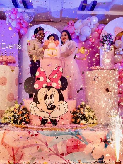 The perfect shot! This photo captures the happy family during the cake-cutting moment at a Minnie Mouse-themed birthday party, complete with sparklers and a stunning balloon and cake table setup.