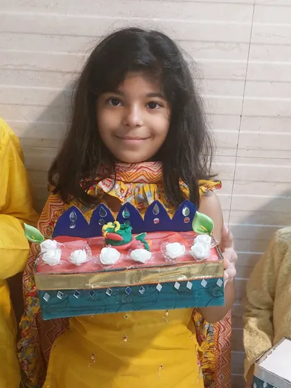 A smiling girl holds up her beautifully decorated festive box. The intricate details and vibrant colors showcase her creativity and the skills she learned during the session.