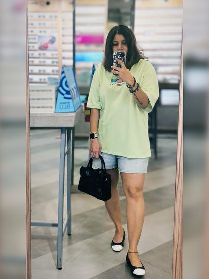 A low-key outfit check in the mirror. A pastel green oversized t-shirt paired with denim shorts is a simple and comfortable choice for a casual Tuesday.
