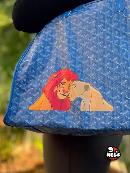 A close-up of the beautiful, hand-painted Simba and Nala artwork on the Goyard bag.