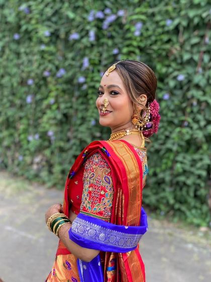 A side view of a bride in her red and blue Nauvari saree. The intricate updo is decorated with flowers and a traditional hair accessory.