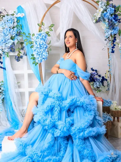 A radiant solo portrait of the mom-to-be in a magnificent ruffled blue gown. Seated against a floral arch, her joyful expression is the centerpiece of this beautiful shot.