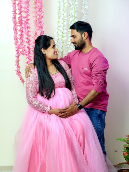 A happy couple portrait from a studio session. The mother-to-be is glowing in a pink tulle gown, sharing a loving gaze with her partner.