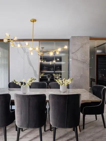 The dining area in the AMARA residence is defined by its clean lines and use of natural materials. A modern brass chandelier hangs above the marble table, and mirrored panels reflect light, making the space feel bright and elegant.