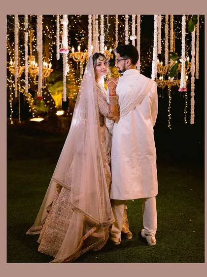 The bride looks back over her shoulder, sharing a sweet moment with her groom under a canopy of fairy lights. A classic and romantic nighttime portrait.