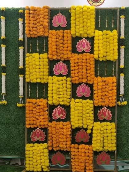 A vibrant backdrop for a Half Saree function, featuring a checkerboard pattern of yellow and orange marigolds on a green grass wall, accented with lotus cutouts.