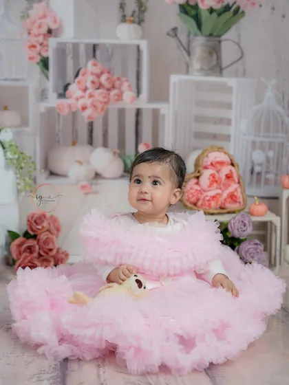 A full portrait in her beautiful pink dress, surrounded by a rustic setup of white crates and pink flowers.