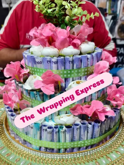 A three-tier cash cake decorated with soft pink flowers and a green ribbon. I can adjust the decorations to be as simple or elaborate as you like.