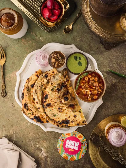 A top-down shot capturing a classic North Indian meal. I used a dark, moody style to highlight the rich textures of the garlic naan and the deep colors of the chole, creating a rustic and soulful image for Chew Chapad's menu.
