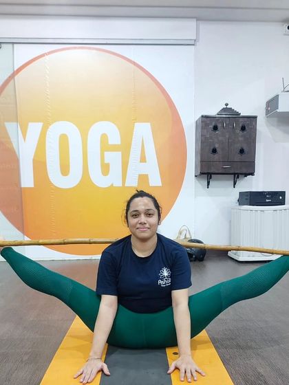 A student uses a stick to maintain balance and alignment in a wide-legged seated forward fold, Upavistha Konasana.
