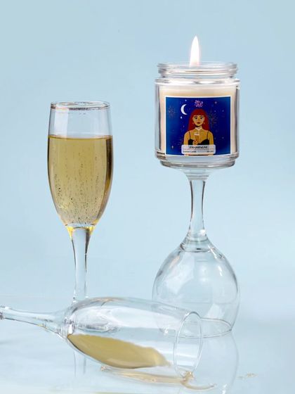 A creative and slightly playful shot, with the champagne candle balanced on an inverted wine glass. The spilled champagne adds a touch of drama and spontaneity to the scene.