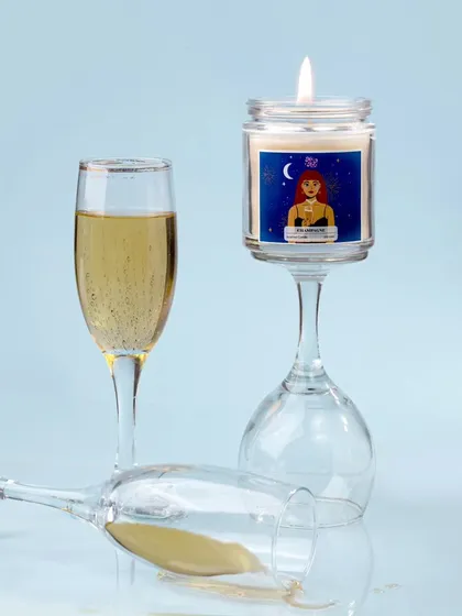 A creative and slightly playful shot, with the champagne candle balanced on an inverted wine glass. The spilled champagne adds a touch of drama and spontaneity to the scene.