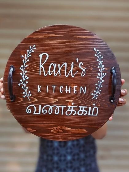 A personalized kitchen board that doubles as a beautiful piece of decor. This round serving tray for "Rani's Kitchen" features elegant lettering and a warm "Vanakkam" greeting in Tamil.