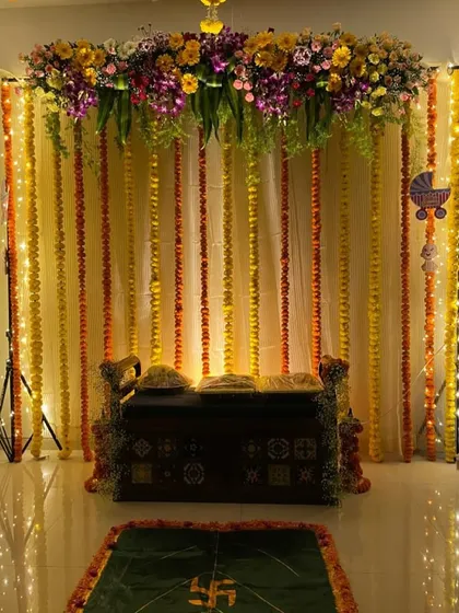 A beautiful and traditional home Ganpati decor, using classic marigold strings and a colorful floral topper to create a festive atmosphere.