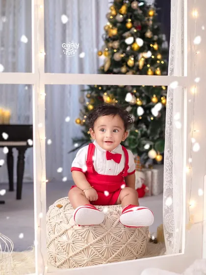 A little boy sits by the window, enjoying the view of the snow and the beautifully decorated Christmas tree.