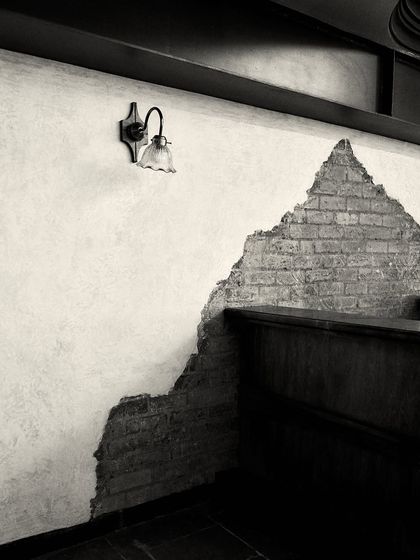 A vintage-style wall sconce illuminates a section of the textured wall, showcasing the interplay of light, shadow, and raw materials.