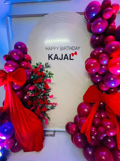 A romantic and elegant birthday theme for Kajal. The decor features a rich red color palette with beautiful rose arrangements and balloon garlands flanking a personalized backdrop.