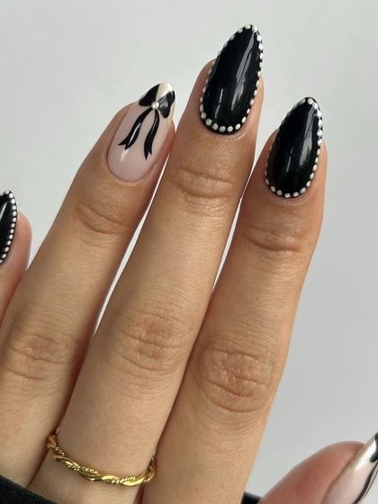 Nail inspiration showing a chic black coquette design with pearl-dotted borders and a bow accent.